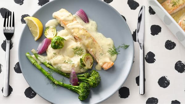 Na ubruse s puntíky leží šedý talíř FÄRGKLAR s porcí lososa s bramborovou kaší a citronovo–koprovou omáčkou vedle zapékací misky IKEA 365+ s dalšími porcemi lososa.