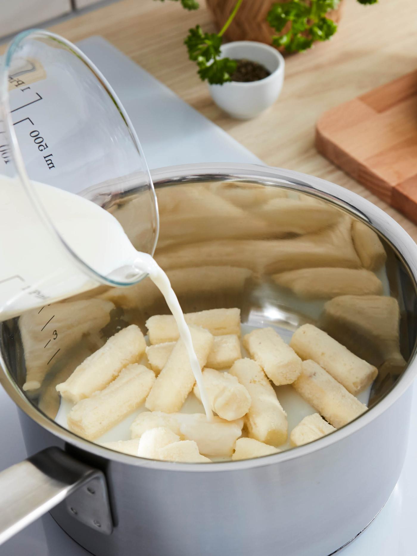 Na válečky mražené bramborové kaše v rendlíku HEMKOMST teče mléko z odměrky VARDAGEN.