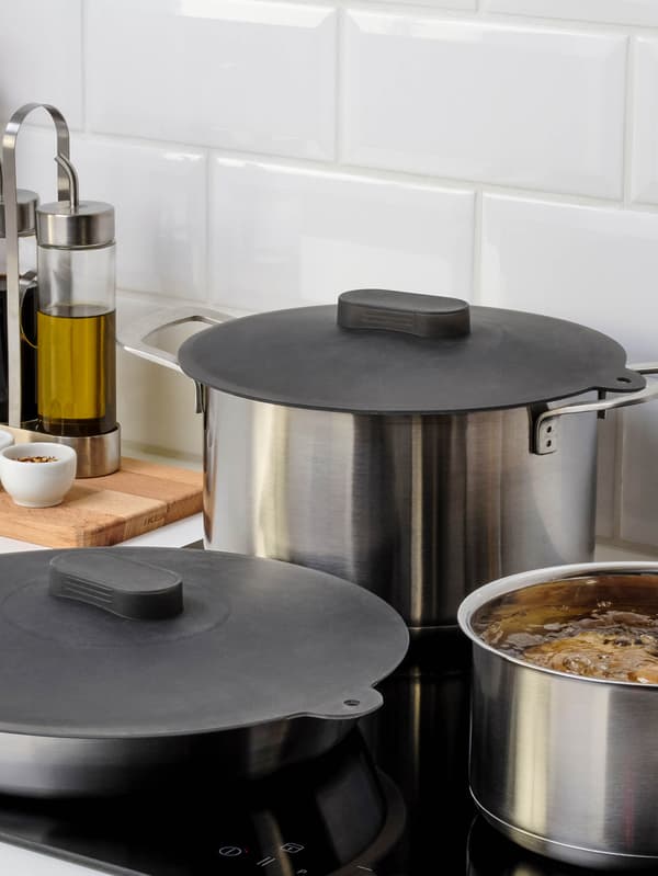 Na varnej doske stojí hrniec bez pokrievky a hrniec a panvica so sivými silikónovými pokrievkami KLOCKREN. 