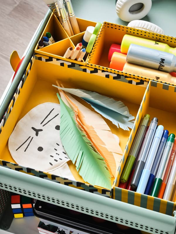 Na vozíku ÖVNING sú v žltých škatuliach LYSMASK uložené fixky a temperové farby MÅLA.