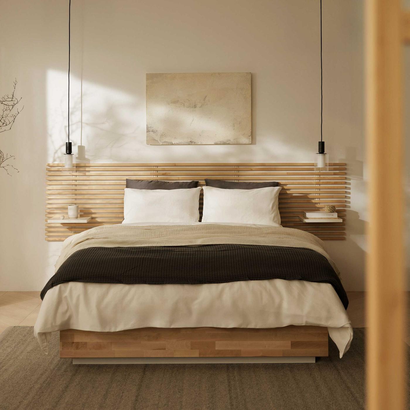 ナチュラルウッドのフレームにホワイト系の寝具とダークグレーのブランケット・クッションでまとめ、清潔感と落ち着きのあるベッドルーム。