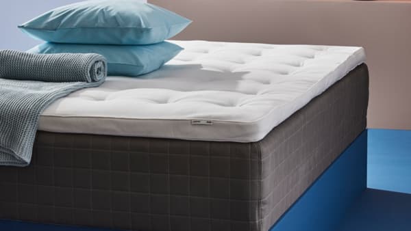 Naddušek stoji na krevetu sa jastucima i prekrivačem