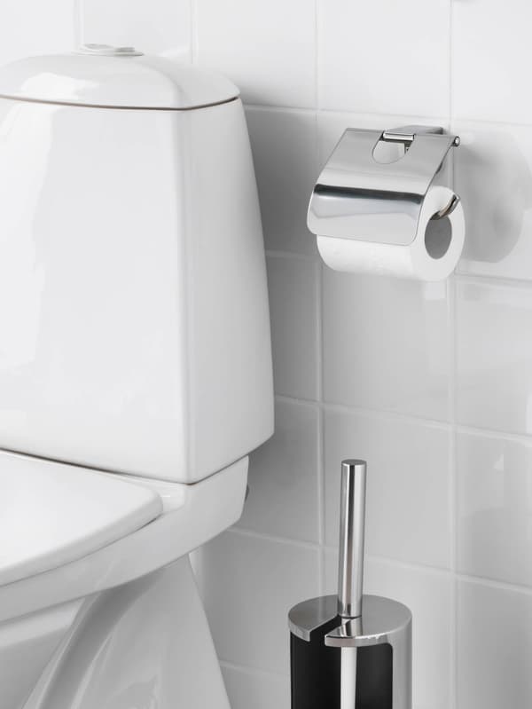 Nádržka bielej toalety pred bielo vykachličkovanou stenou.