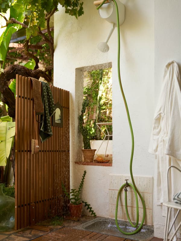 NÄMMARÖ paraván egy falra szerelt, házilag készült zuhany mellett, amely egy locsolótömlőből és egy SALLADSKÅL locsolókannából áll.