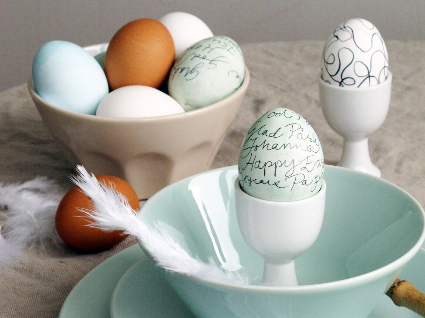 Närbild på ägg i olika färger som vi skrivit och ritat på efter att vi färgat äggen. Äggen står i äggkoppar och ligger i en skål.