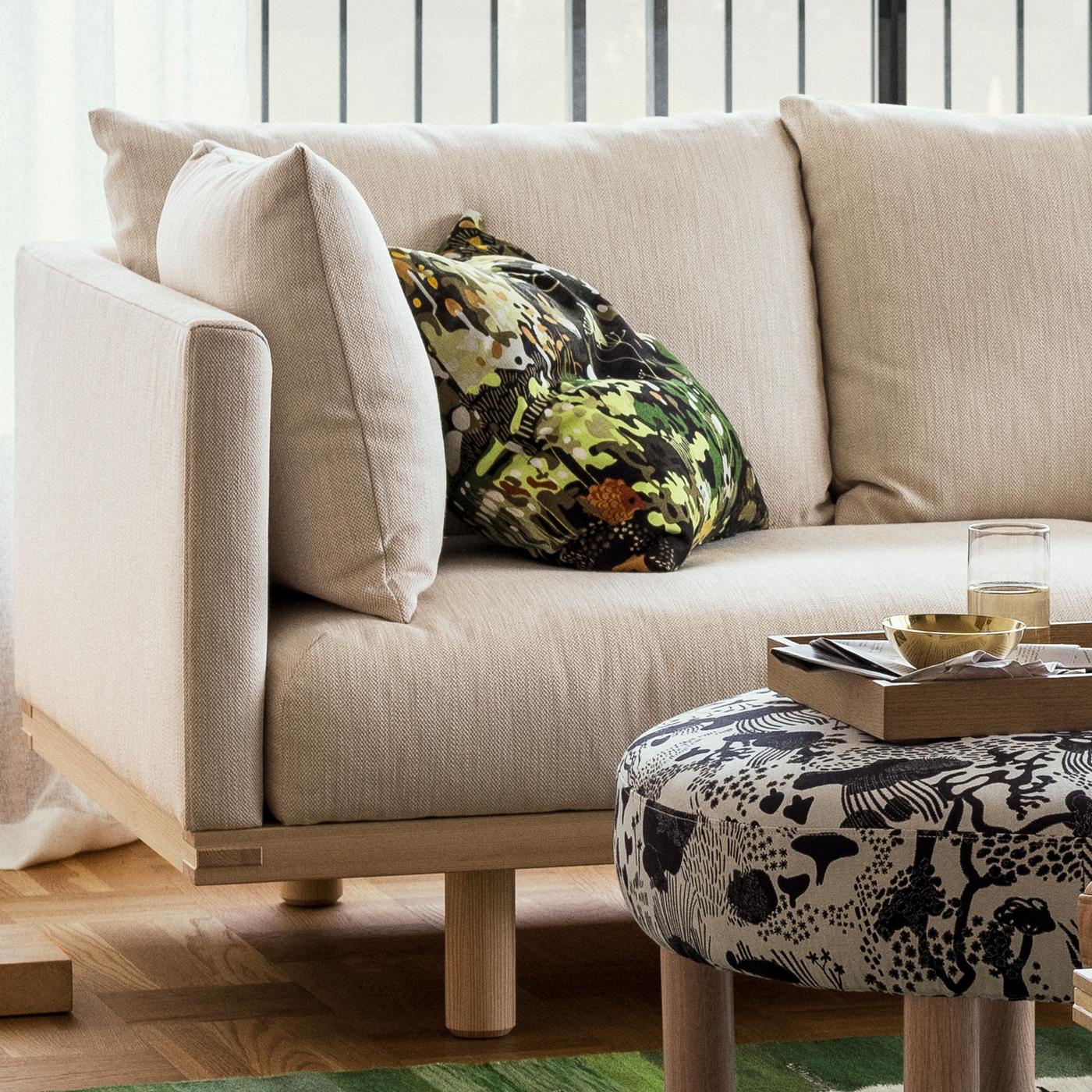 Närbild på en beige STOCKHOLM soffa med en vit- och svarmönstrad, rund fotpall framför. 