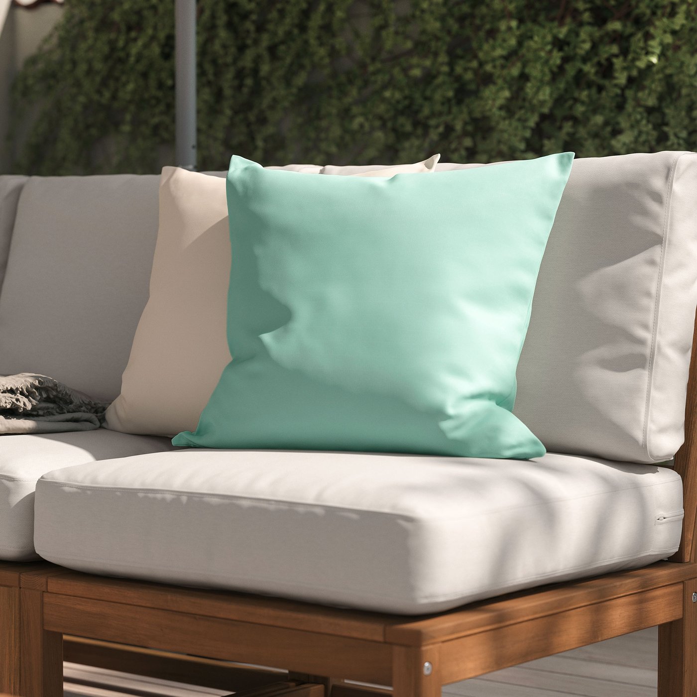 Närbild på en ljusturkos utomhuskudde i en utesoffa i trä med beige dynor.