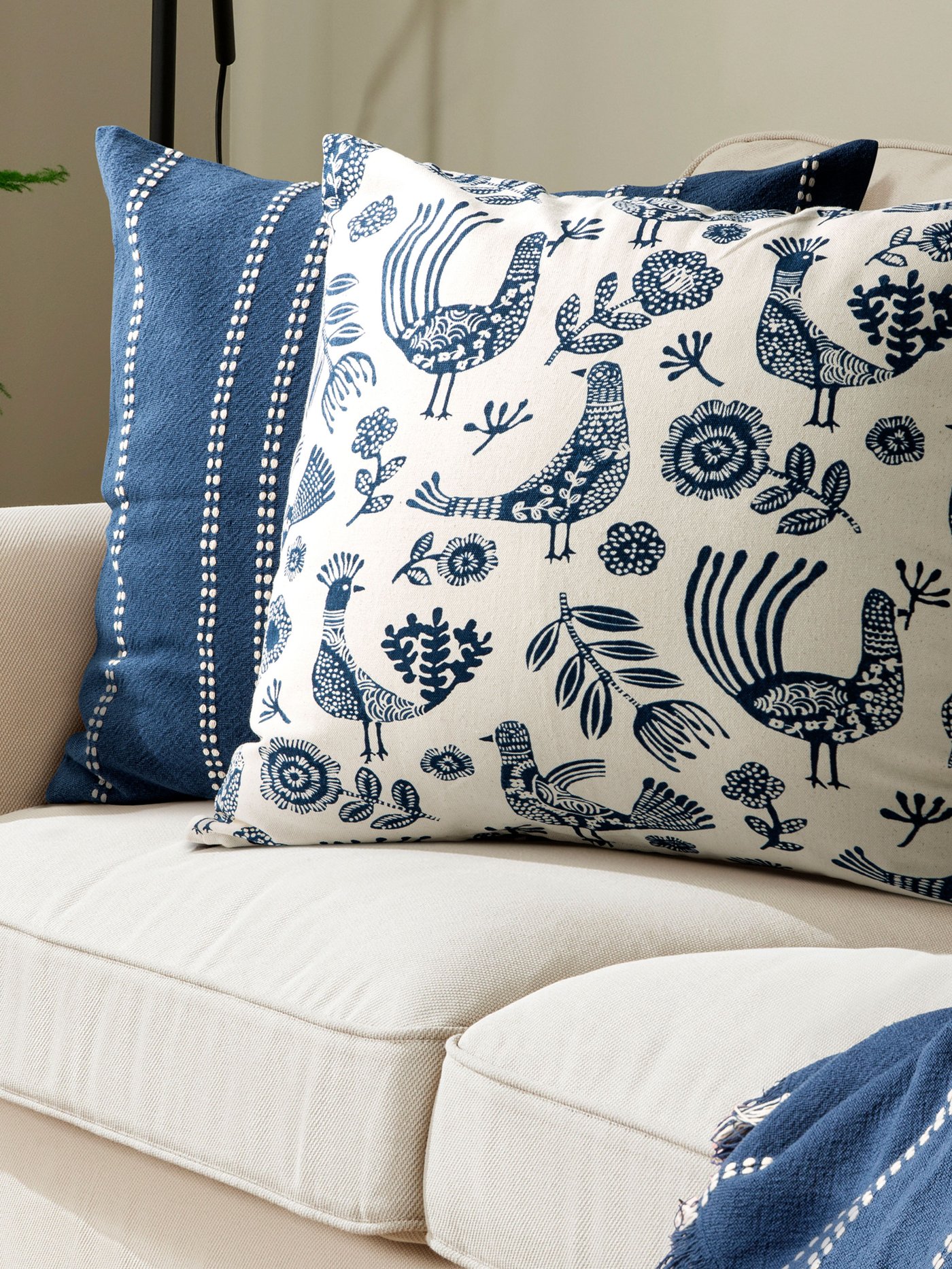 Närbild på en vit kudde med blått mönster rillsammans med en blå och vitrandig kudde i en beige soffa. 