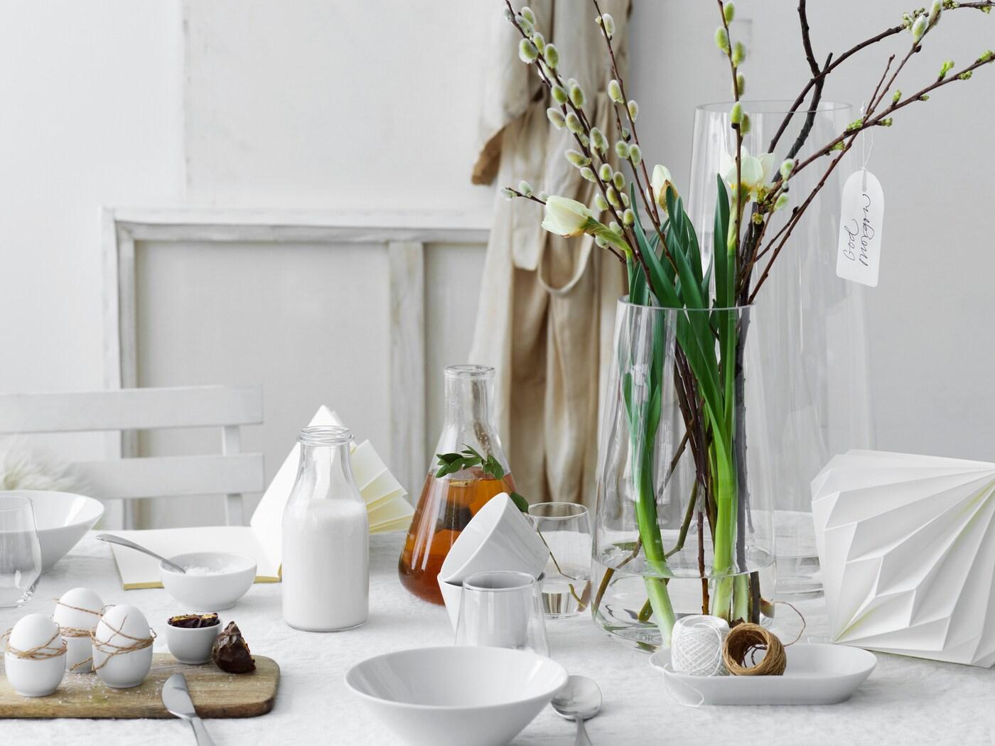 Närbild på ett vitt bord med vårblommor i en genomskinlig vas.