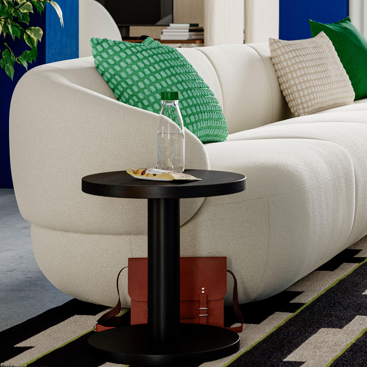 Närbild på LILLESÄTER vit soffa med en grön kudde där ett svart runt sidobord står vid ena armstödet. 