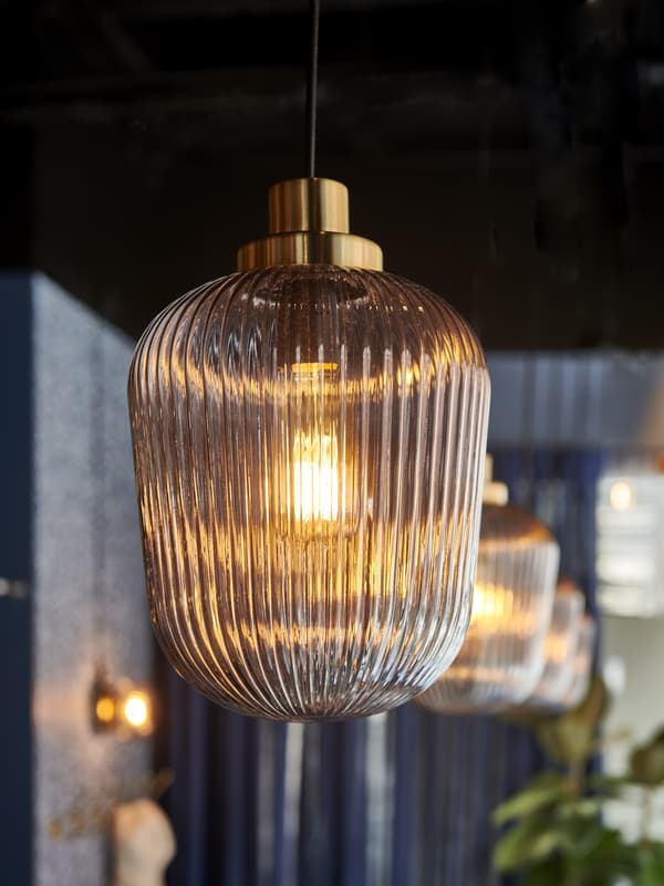 Närbild på SOLKLINT taklampa med räfflad glaskupa och glödande glödlampa, fler lampor i bakgrunden skapar varm stämning.
