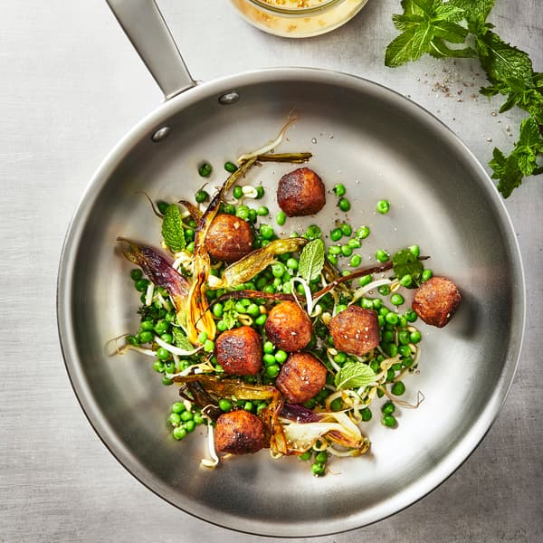 Närbild på stekpanna med åtta köttbullar tillsammans med ärtor och stekt kål.