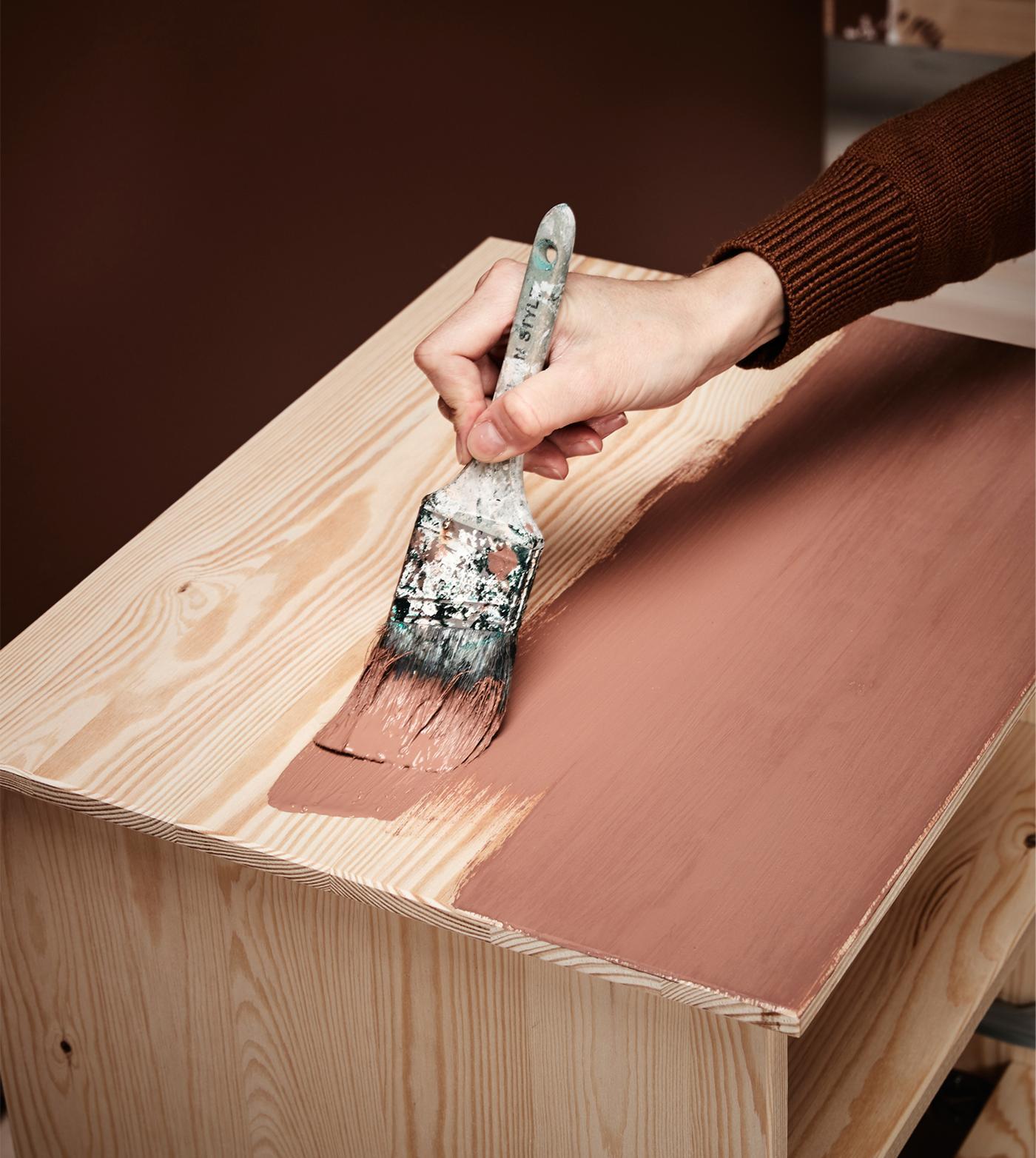 Nærbillede af en hånd der maler en træoverflade.
