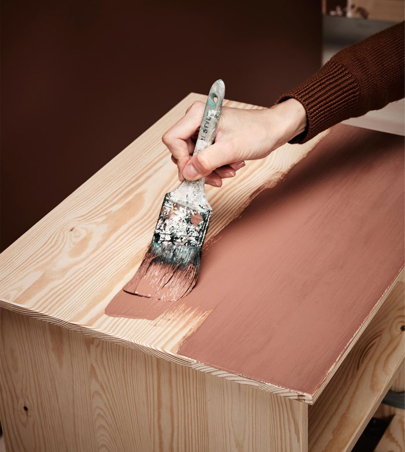 Nærbillede af en hånd der maler en træoverflade.