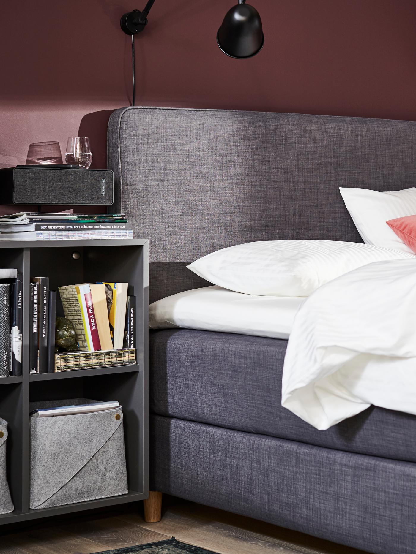 Nærbillede af seng med blød sengegavl og et sengebord med bøger ved siden af.