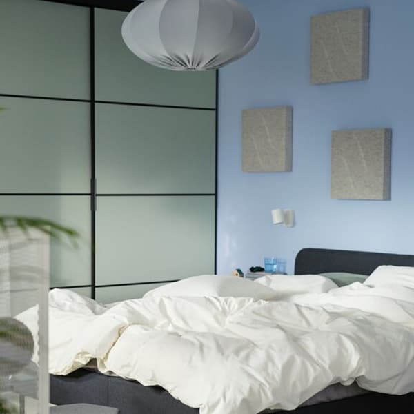 NÄVERHÄGG noise-absorbing panels fixed to a blue wall over an unmade bed.