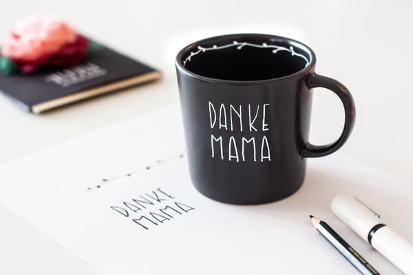 Nahaufnahme der individuell beschriebenen Tasse. Sie ist schwarz und mit weißemPorzellanstift steht 