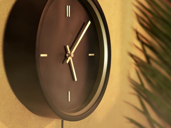 Nahaufnahme der schwarzen STURSK Wanduhr mit goldfarbenen Details an einer goldbraun gestrichenen Wand.