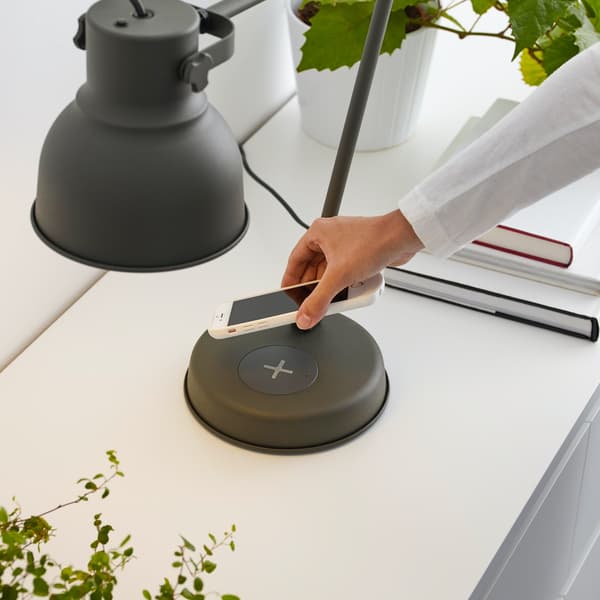 Nahaufnahme einer Hand, die ein Mobiltelefon auf eine kabellose Ladestation legt. Daneben liegt eine Brille.