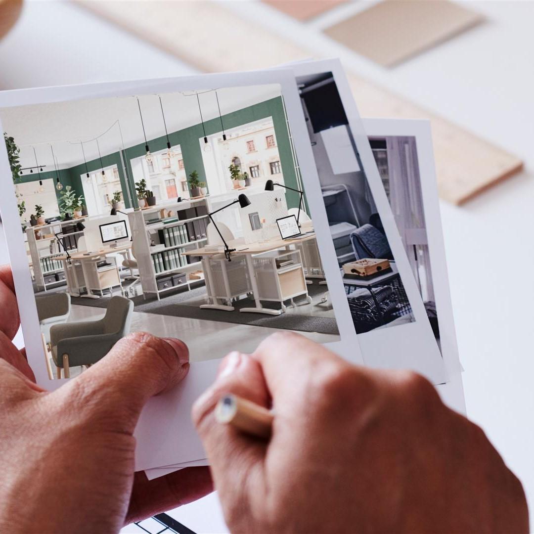 Nahaufnahme einer Hand mit Polaroids von Büroräumen, in der anderen and hält die Person einen Stift