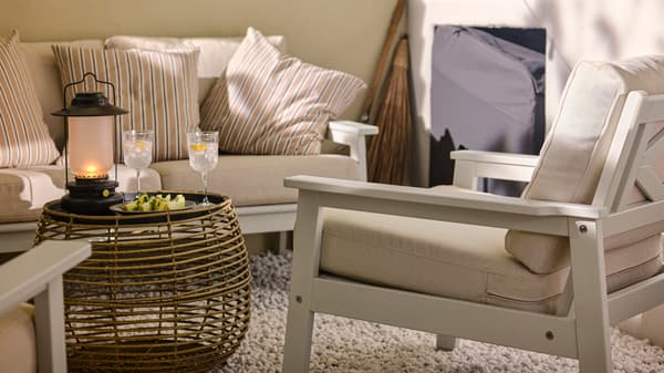 Nahaufnahme eines BONDHOLMEN 2er-Sofas für draußen mit zwei gestreiften Kissen und einem FÅLSKÄR Couchtisch. Auf dem Tisch stehen Gläser und eine Laterne.