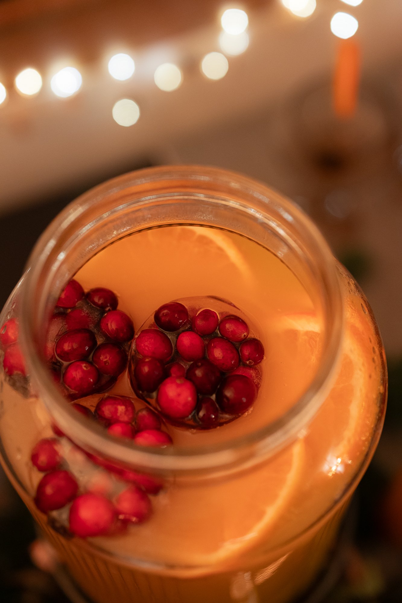 Nahaufnahme eines Glasbechers, gefüllt mit einem warmen Getränk, garniert mit Cranberries und Orangenscheiben. Sanftes, warmes Licht sorgt für eine gemütliche, festliche Atmosphäre.