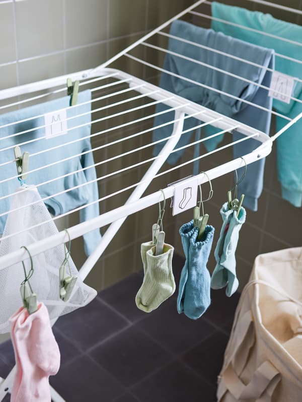Nahaufnahme eines MULIG Wäschetrockners, an dem Kleidung und Socken in verschiedenen Farben hängen, die mit SLIBB Wäscheklammern befestigt wurden.
