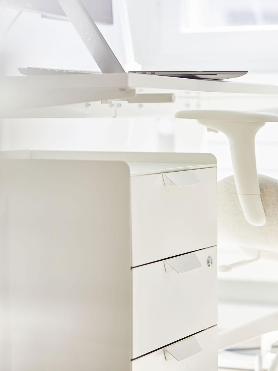 Nahaufnahme eines weissen Rollcontainers mit Schubladen, der unter einem weissen Schreibtisch steht. 