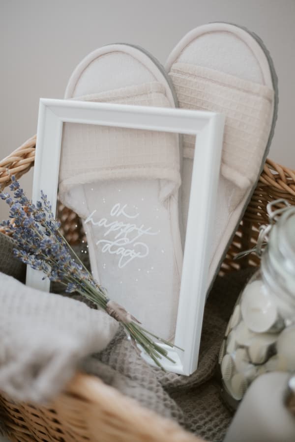 Nahaufnahme von einem Geschenkkorb mit Fokus auf einem weißen Bilderrahmen. Die Rückseite wurde entfernt sodass nur das Glas im Rahmen hängt. Auf dem Glas wurde mit weißem Lackstift 