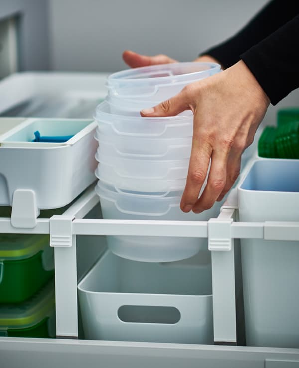 Nahaufnahme von jemandem, der Vorratsdosen aus Kunststoff in eine Schublade mit angepassten Trennstegen setzt