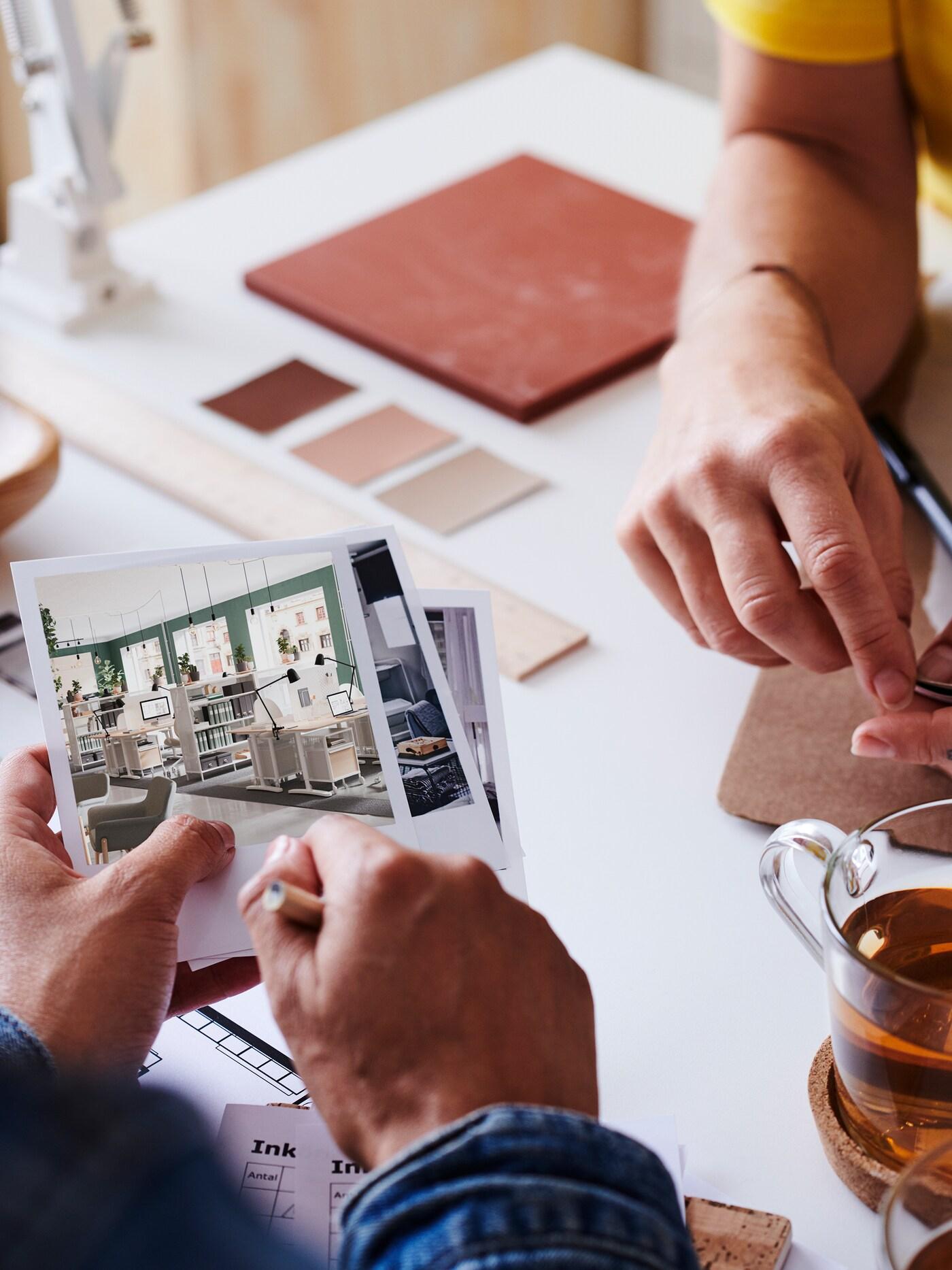 Nahaufnahme von zwei Personen, die Fotos von Inneneinrichtungen und Mustern auf einem weißen Tisch betrachten.