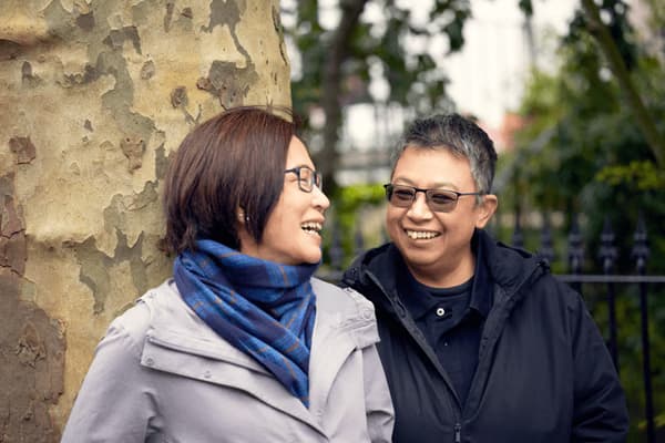 Nancy and her partner May standing outside underneath a large tree smiling at each other.