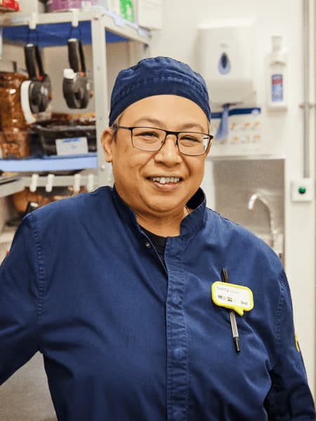 Nancy in her work uniform standing in the IKEA FOOD kitchen where she works.