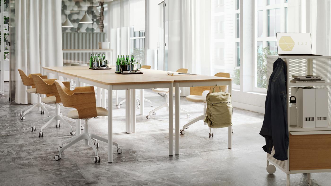 Napfényes tárgyaló asztalokkal és székekkel világos fából és fehér tónusokban, egyszínű, fehér függönyökkel és egy üvegfallal.