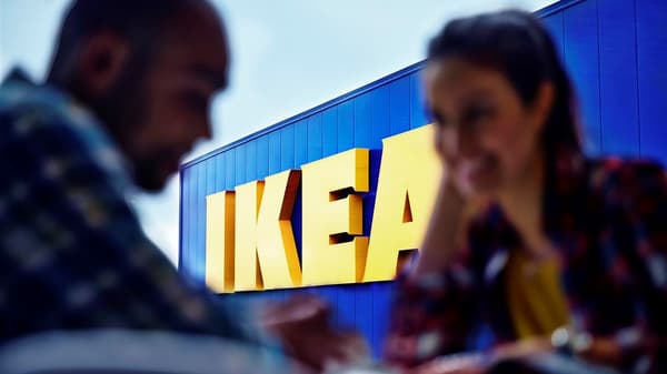 Napis IKEA na sklepie IKEA. Na pierwszym planie niewyraźne postacie kobiety i mężczyzny.