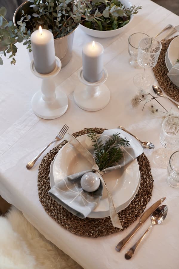Napkins decorated with a small fir branch, placed on a plate, with cutlery and candles next to it.