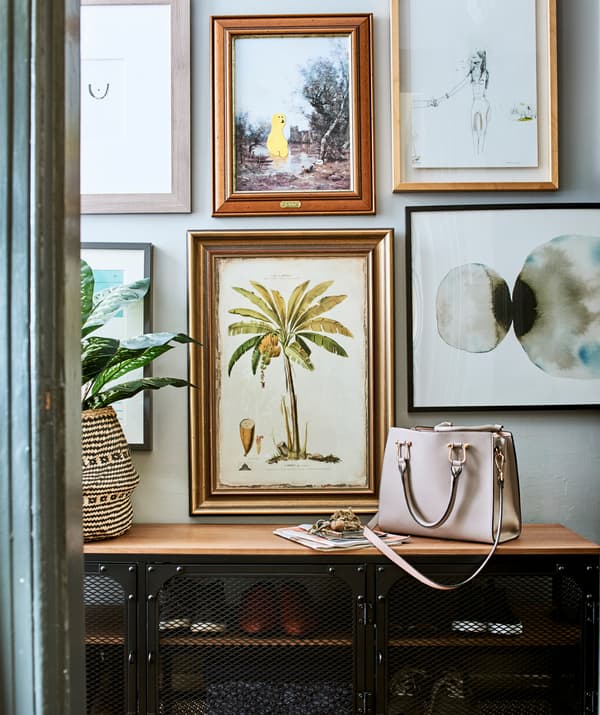 Nástenná galéria z rôznych rámov nad čiernou kovovou skrinkou s dreveným povrchom.