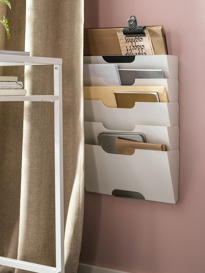 Nástěnný pořadač IKEA KVISSLE s několika přihrádkami na dokumenty a dopisy, namontovaný na růžové stěně vedle stolu.