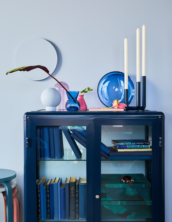 Nature morte décorative composée de vases, de plats et de globes en verre coloré, placés sur le dessus d’une armoire bleu foncé, le tout de chez IKEA.
