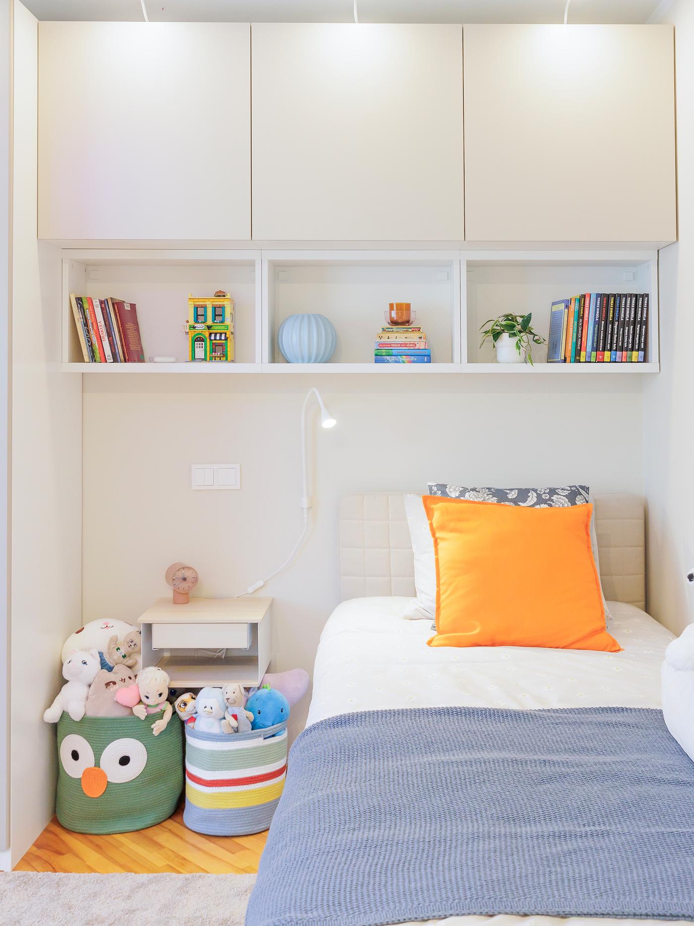 Neatly organised white cabinets and shelves above the bed, filled with colourful books and small toys.