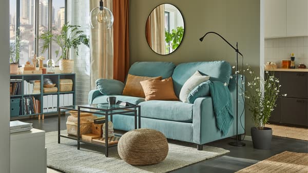 Nesting tables in front of a high-back light turquoise sofa, open cabinets are by the window with books, baskets and files.
