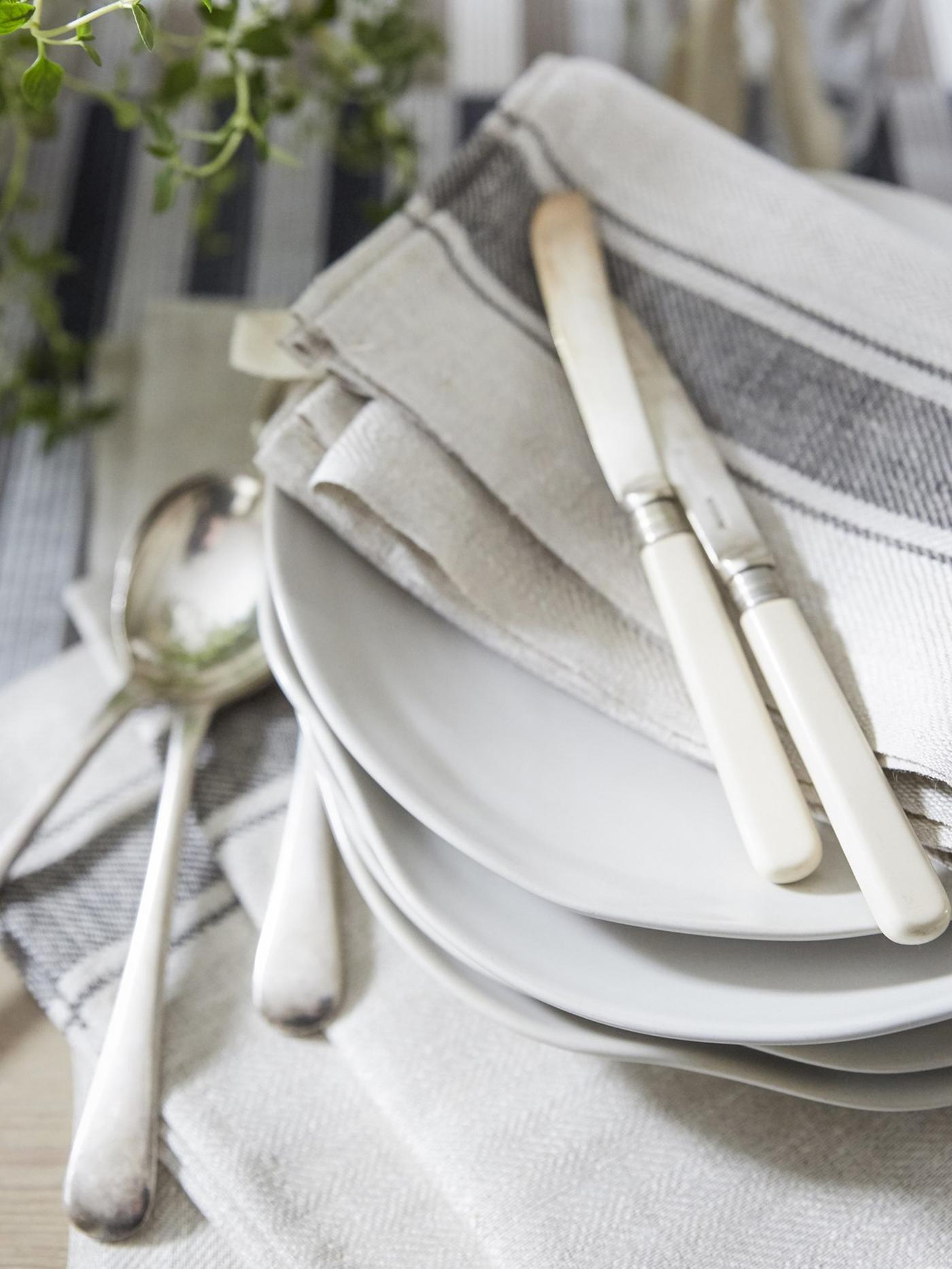Neutral-colored cotton napkins and cutlery on a stack of white plates.