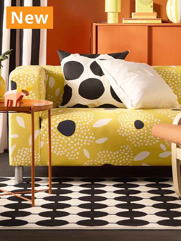 NEW IKEA product. A KLIPPAN Tingetorp yellow/white/floral pattern sofa in living room with orange GLADOM table and VANDPLATS rug.