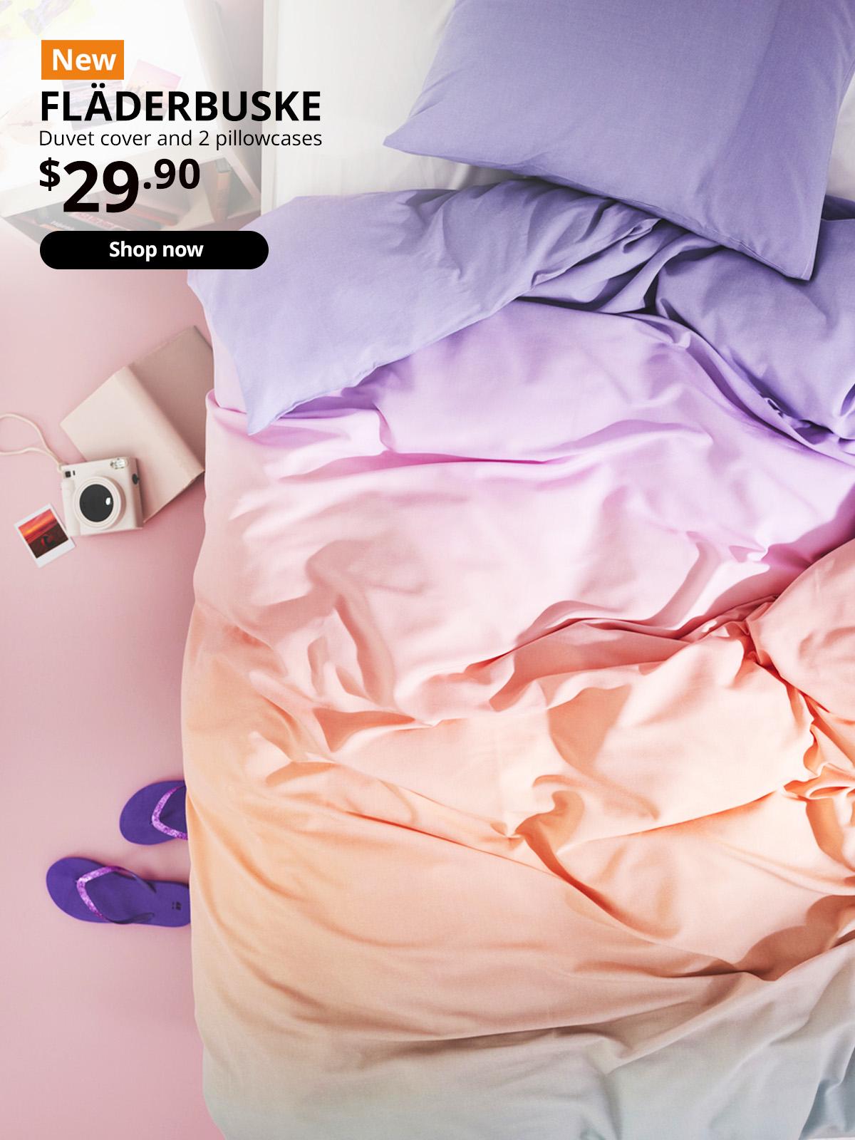 New IKEA product. FLÄDERBUSKE duvet cover and 2 pillowcases (200x200/50x80 cm) in gradient shades of purple to pink, la over a queen sized bed. Price: $29.90.