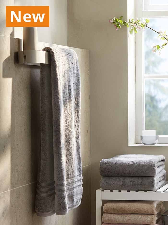 NEW IKEA product. FLORSJÖN towel rail in beige mounted to bathroom wall, with dark grey BROGKLIM bath towel hanging over it in the bathroom.