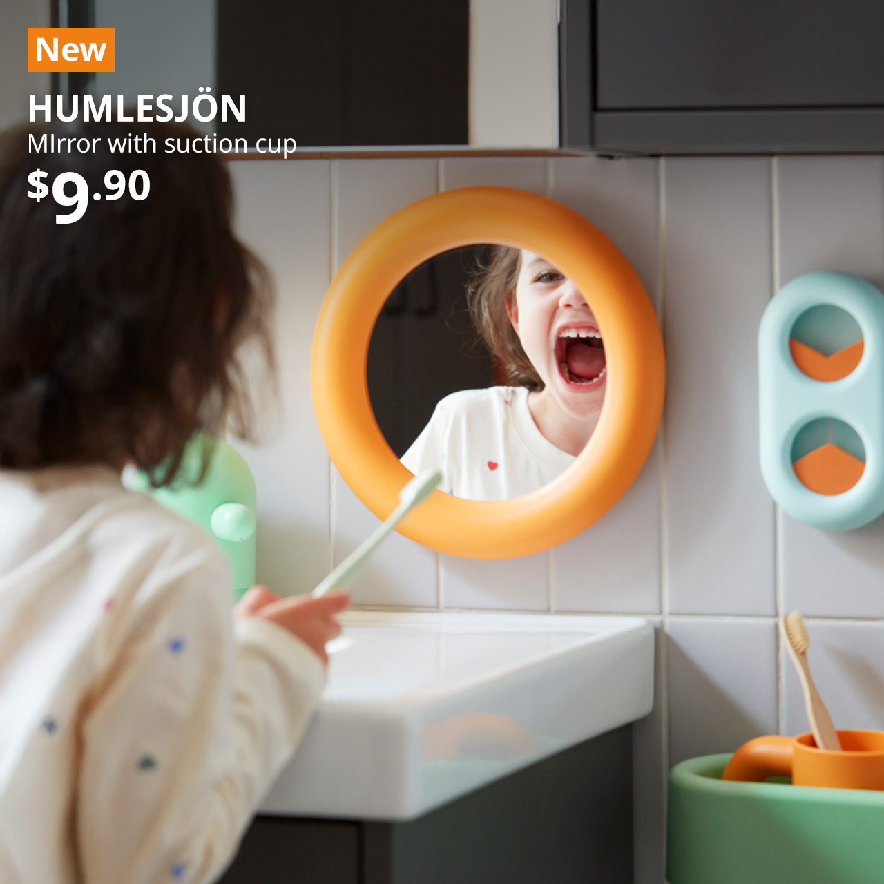 NEW tag. A orange HUMLESJÖN mirror with suction cup is placed above the bathroom vanity while a child is looking into the . Black text on image reads "BACKMÅRA, Bath mat, 40x60 cm. Price: $7.50"