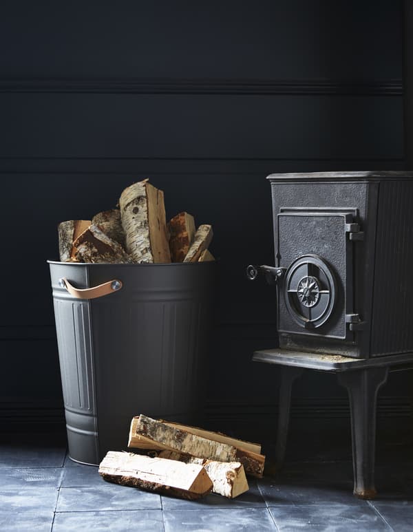 Next to a fireplace, a KNODD bin with leather handles holds firewood.