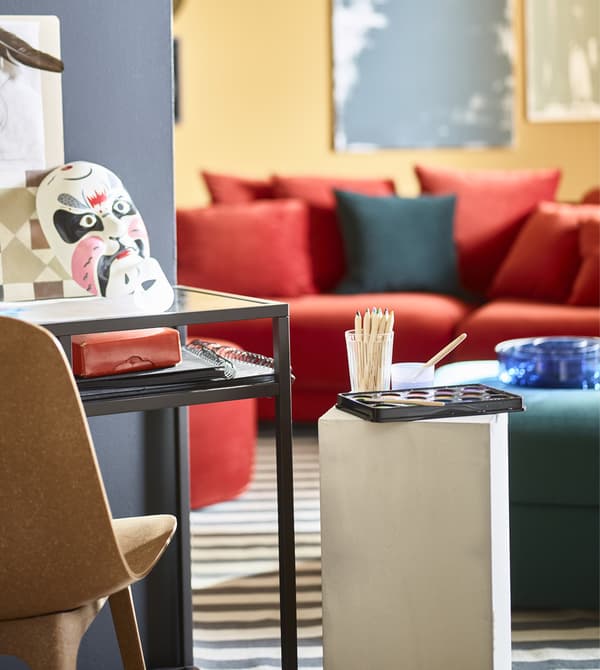Next to a workspace, a pedestal holds a paint palette and coloured pencils.