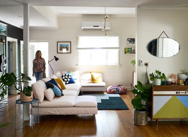 Nici เดินเข้าไปในห้องนั่งเล่นสีขาวที่มีโซฟาสีชมพูอ่อนขนาดใหญ่ พรมสีน้ำเงิน และตู้ไซด์บอร์ดสไตล์วินเทจ