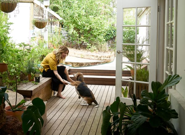 Nici และสุนัขของเธอนั่งอยู่บนเฉลียงไม้ในสวนด้านนอกประตูสีขาว